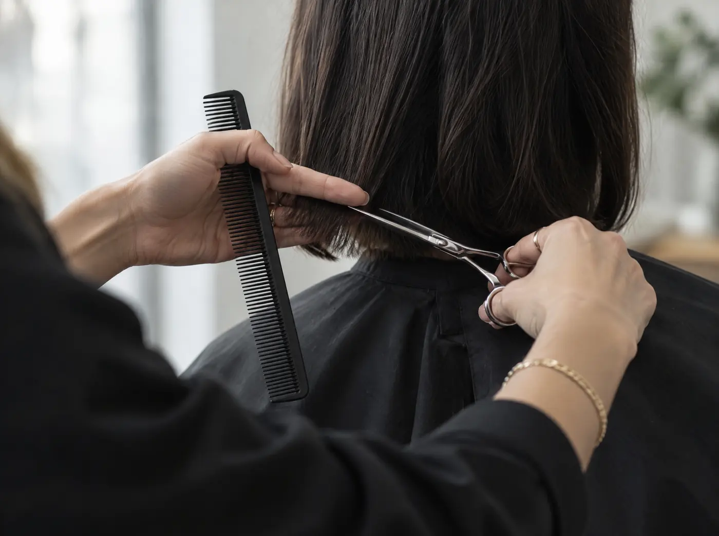 Une coiffeuse coupe au ciseau les cheveux d’une cliente, vue de dos